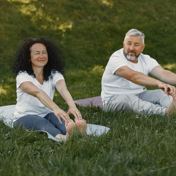 Person smiling and stretching outdoors in a green park at sunrise.